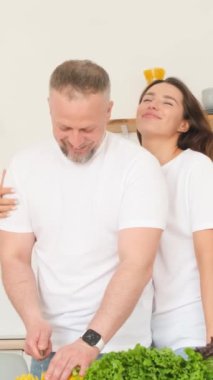 Genç adam ve kadın evde sağlıklı yemek pişirirken gülüyorlar. Mutlu çift mutfakta birlikte yemek yapmaya bayılır. Dikey video