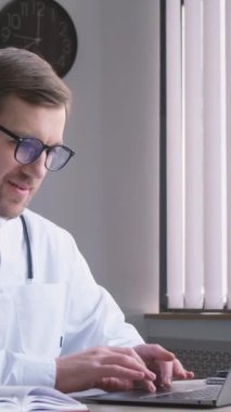 Gözlüklü ve üniformalı ciddi bir doktor bilgisayardaki ofisinde çalışıyor. Doktorun elektronik işi bu. Doktor psikoterapist, iş yerinde kardiyolog. Dikey video