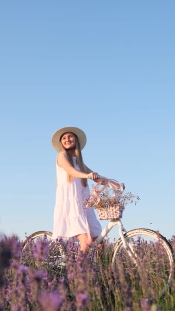 落ち着いた青空に向かって自転車で立っている紫色のラベンダーフィールドの女性の肖像画 フィールドでの写真セッション 写真セッションのための装飾 バーティカルビデオ — ストック動画