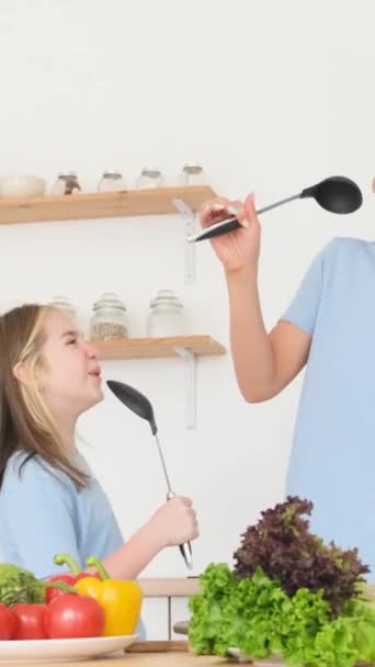 笑顔の母親と娘が自宅の台所でスプーンと歌っている キッチンで料理をする女性と女の子 一緒に幸せな家族 バーティカルビデオ — ストック動画
