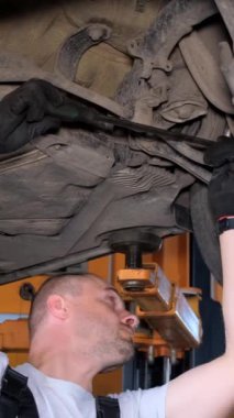 Araba tamircisi arabanın şasisine teşhis koyuyor. Tamir istasyonunda yükseltilmiş araba. Araba servis istasyonu. Dikey video