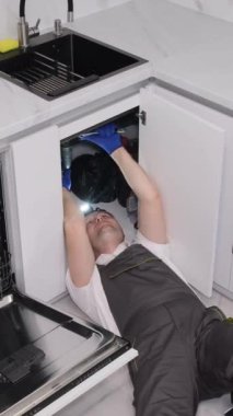 Bir tamirci lavabonun altından su sızıntısını tamir ediyor. Bir muslukçu boru tamir etmek için lavabonun altında yatıyor. Dikey video