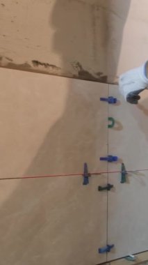 Duvara seramik fayanslar sergiliyor. Usta duvarın seviyesini ölçer. Dikey video.