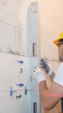 İnşaatçı seramik fayansların montajı sırasında duvarın dikey sapmasını ölçer. Kabarcık seviyesinde cetvel, ölçme ve dengeleme konsepti. Dikey video