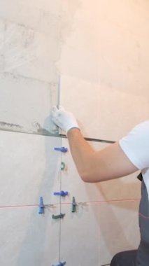 Döşeme ustası banyonun duvarına fayans döşeme işini yapıyor. Döşeme işe yarıyor. Dikey video.