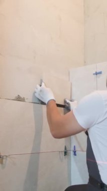 Döşeme işe yarıyor. Tiler, banyo duvarına fayans döşeme işini yürütür. Tiler, duvara büyük ölçekli fayanslar yerleştirir. Dikey video