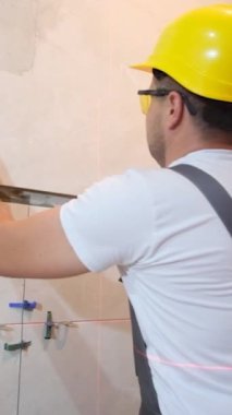 Bir tiler banyodaki bir duvara seramik fayanslar sergiler. Tulum ustası duvara seramik fayanslar koyar. Dikey video