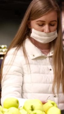 Tıbbi maskeli genç bir kadın Covid-19 Coronavirus salgını sırasında süpermarketten yiyecek alıyor. Kadın karantina ve kendini izole etme süresince yiyecek depoluyor. Dikey video