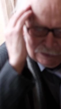 Pencerenin yanındaki bir odada oturan yaşlı, gri saçlı bir adamın başı ağrıyor, şakaklarını ovuyor, migren ve depresyon geçiriyor. Dikey video