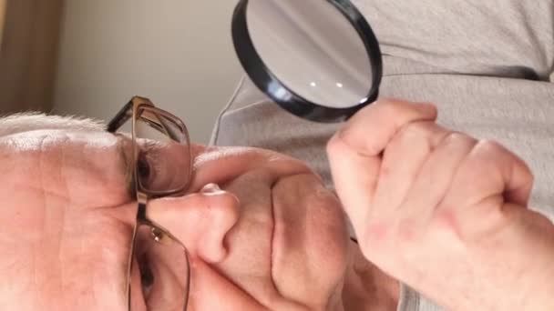 Een Oudere Man Met Slecht Gezichtsvermogen Gebruikt Een Vergrootglas Terwijl — Stockvideo