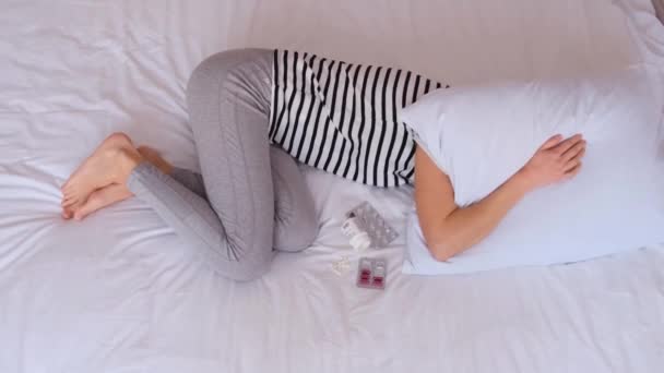 病気の女性は白いベッドの上に横たわり 白い枕で頭を覆っている 痛みによる苦しみ 彼女には問題がある コビドとの分離 バーティカルビデオ — ストック動画
