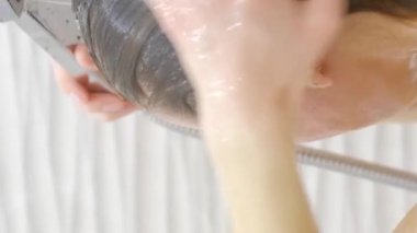 Uzun saçlarla ilgilenen, banyoda duş alan bir kadın. Kapatın. Dikey video