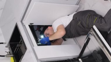 Mutfakta yerde yatan bir tesisatçı lavabo yerleştirir. Tesisatçı işi. Dikey video