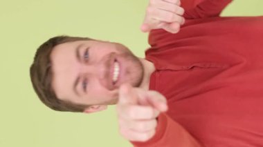 Yakışıklı bir adam kamerayı işaret eder, stüdyonun arka planında durur ve samimi bir şekilde gülümser. Bir adamın samimi, neşeli duyguları. Dikey video