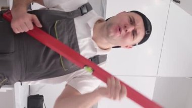 Komik ve eğlenceli mutfak mobilyası derleyicisi inşaat seviyesinde gitar çalma simülasyonu yapıyor. Avrupa görünümlü mutlu genç bir işçi. Dikey video