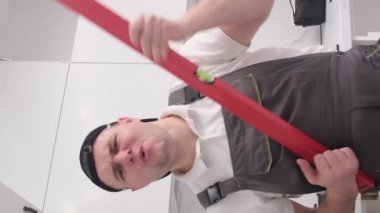 Komik ve eğlenceli mutfak mobilyası derleyicisi inşaat seviyesinde gitar çalma simülasyonu yapıyor. Avrupa görünümlü mutlu genç bir işçi. Dikey video
