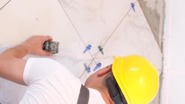 建筑商把瓷砖铺在地板上 穿着制服和头盔的专业工匠 铺设漂亮的白色瓷砖 垂直录像 — 图库视频影像