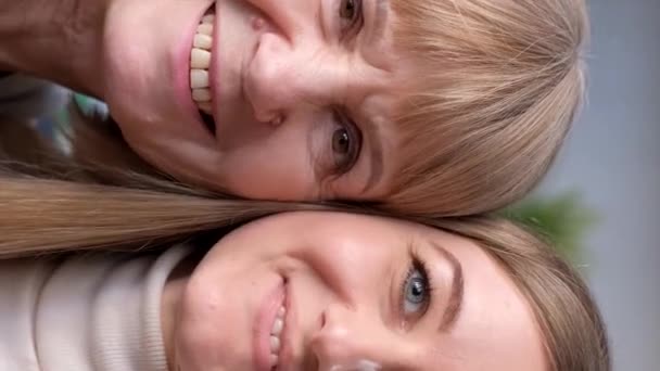 一个漂亮的金发姑娘和她妈妈的画像 他们看着相机笑着 快乐的家庭在家里休息 垂直录像 — 图库视频影像