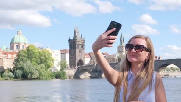 ブロンドの女性は プラハの街のパノラマを持つスマートフォンでセルフィーを取ります チェコ — ストック動画
