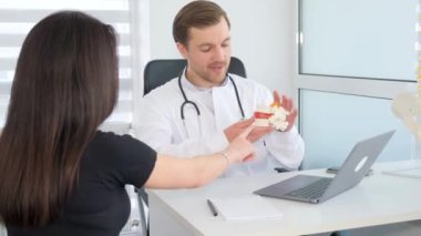 Ortopedi doktoruyla konsültasyonda olan esmer bir kadın. Doktor, çene modeli için müşteriye danışıyor. Görsel denetim. İskeletin bir parçası.
