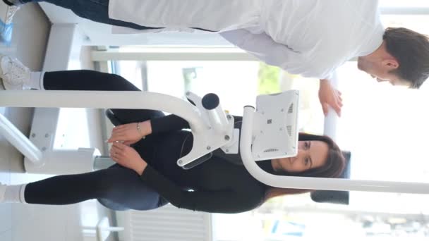 垂直录像 身穿制服的年轻脊椎专家会会诊运动健康中心的病人 背部和颈部运动器械上的女病人 骨坏死及脊柱侧弯的治疗 — 图库视频影像