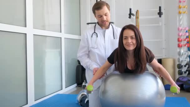 一位专业的年轻脊椎学家正在康复中心教一位妇女 体操球上的女人 受伤后康复 — 图库视频影像
