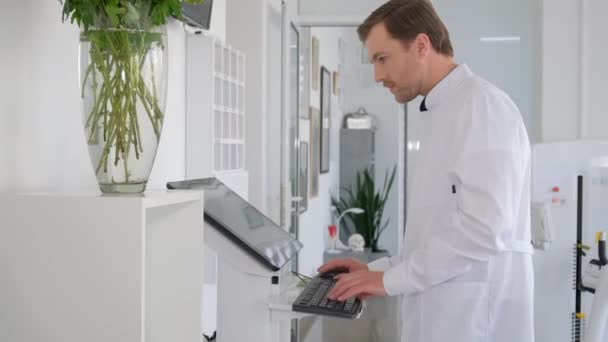 身穿白色制服的年轻貌美的医生在现代诊所与白色的内部 医生在电脑前工作 — 图库视频影像