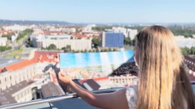 Sarışının elinde Almanya 'nın Dresden şehrinin haritası var. Şehrin manzarasına tepeden bakıyor. Almanya 'da turizm