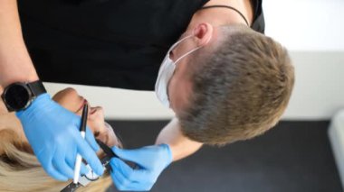 Yüzün üçüncü kısmının cerrahi maskeyle düzeltilmesi. Yüzünde kırışıklıklar, göz kapaklarının kenarları sarkmış. Estetik cerrahın işi. Dikey video