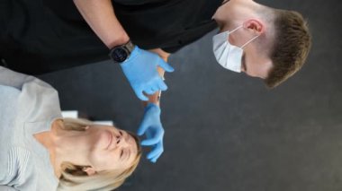 Bir kozmetolog yaşlı bir kadının yüzüne kırışıklık önleyici iğneler yapar. Dikey video.