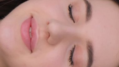 Avrupa görünümlü güzel esmer bir kızın portresi, gözlerini açıyor ve gülüyor. Dikey video