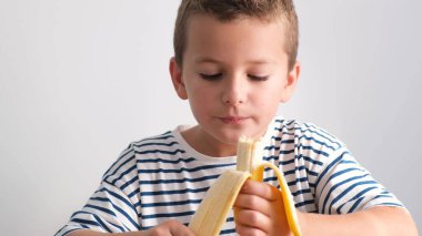 Tatlı küçük bir çocuk beyaz arka planda olgun bir muzu yiyor. Lezzetli tropikal meyveler. Sağlıklı yemek.