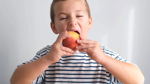 Beautiful baby boy bites a peach. The face of a child eating a healthy snack, ripe fruit. High quality 4k video