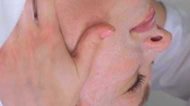 Kozmetik prosedürleri. Bir kozmetolog temizlik prosedürü uygular. Güzellik uzmanı kızın yüzüne maske takmış. Güzellik salonunda yüz bakımı. Dikey video