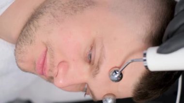 Kozmetik uzmanı iyontoforez prosedürünü gerçekleştiriyor. Erkekler için yüz derisinin gençleşmesi. Ultrasonik deri kaldırma. Dikey video