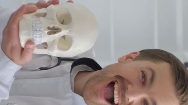 Genç bir doktor ofiste anatomik insan kafatasının bir modelini tutuyor. Bir nörolog çalışırken eğleniyor. Dikey video