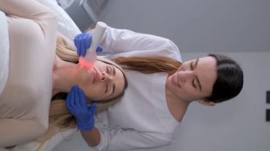 Güzellik salonunda hiyalüronik asit jeliyle yüz fonforezi ameliyatı geçiren bir kadının dikey videosu. Dikey video