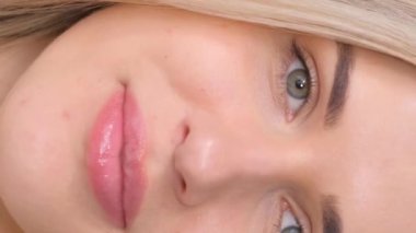 Çok güzel bir kız kameraya bakar ve gülümser. Sarışın portresi. Dikey video.