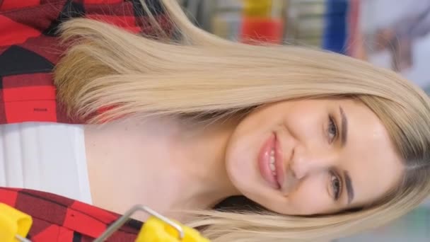 一个漂亮的女孩拿着粉刷滚筒在镜头前笑的画像 硬件商店的促销视频 垂直录像 — 图库视频影像