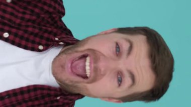 Mutlu kazanan adam, stüdyoda mavi arka planda zafer jesti göstererek seviniyor. Çocuk başarıyı ifade ediyor. Dikey video