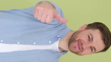 Neşeli, mutlu, gülümseyen genç adam yeşil arka planda parmağını kaldırmış kameraya bakıyor. İnsanların yaşam tarzı konsepti. Dikey video