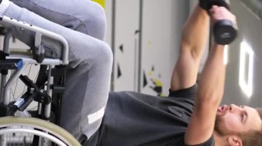 Tekerlekli sandalyedeki engelli bir adam spor salonunda dambılları kaldırıyor. Spor konsepti. Dikey video