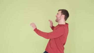 Kırmızı kazaklı yakışıklı genç adam, mutlu ve neşeli dans, gülümseme, hareket, gelişigüzel ve kendinden emin bir şekilde müzik dinliyor..