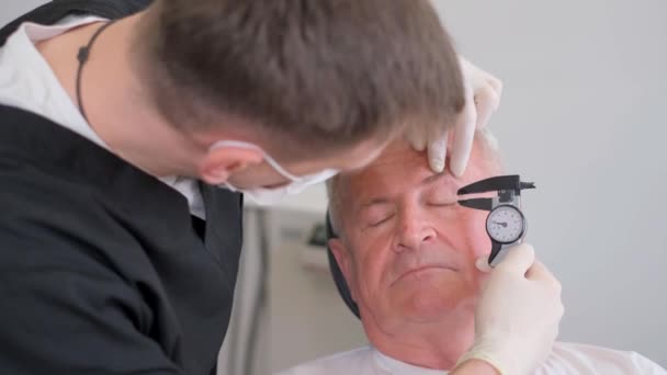 整形外科医生检查眼部凹陷的皮肤 并用卡尺测量 为老年男子的面部整形手术做准备 — 图库视频影像
