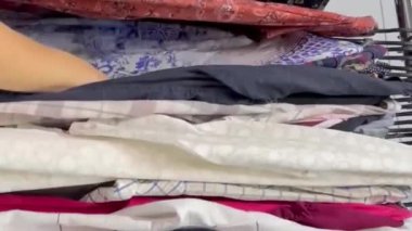 Bir kadın ikinci el dükkanında kıyafet seçer. Kullanılmış giysiler almak. Ortalama çekim planı. Dikey video