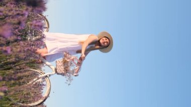 Mor lavanta tarlasında bir kadının portresi durgun mavi bir gökyüzüne karşı duran bir bisikletle duruyordu. Sahada fotoğraf çekimi. Fotoğraf çekimi için dekor. Dikey video