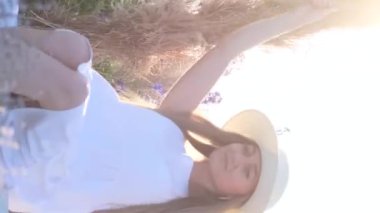 Vahşi çiçeklerin arasında sallanan genç bir bayanın güzel videosu. Sahada fotoğraf çekimi. Güzellik tutkusu. Kendinle uyum içinde. Dikey video