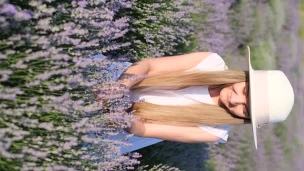 紫色のラベンダーの花に座っている白い帽子の女性の垂直ビデオ ラベンダーの女性 プロヴァンス バーティカルビデオ — ストック動画