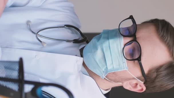 의료용 마스크와 안경을 착용한 의사가 사무실의 넷북에서 일하고 있습니다 현미경을 — 비디오
