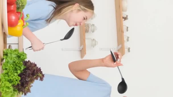 妈妈和女儿在家里厨房里用勺子唱歌 快乐的女人和女孩在厨房里做饭 幸福的家庭在一起 垂直录像 — 图库视频影像